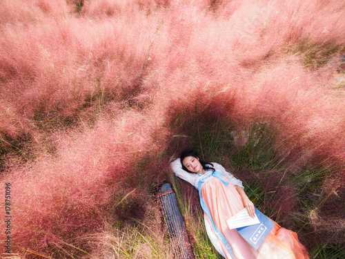 Portrait of beautiful young Chinese woman wearing traditional ancient costume sleeping in the pink hairawn muhly field, aerial view. photo