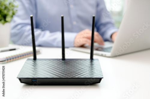 Fotografie Wireless router and man using a laptop in office