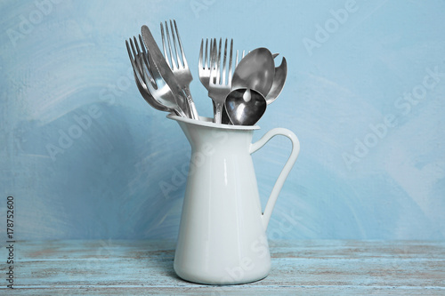 Tableau sur toile Set of metal cutlery in jug on table against blue wall