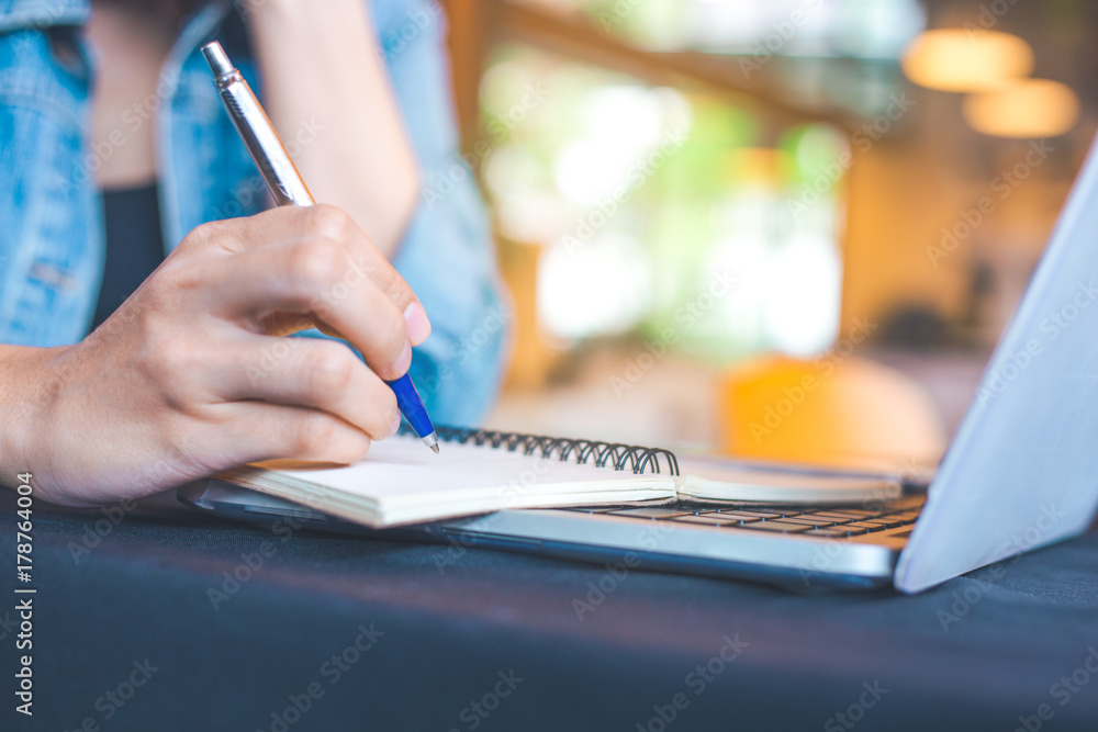 Woman hand works in a laptop computer and is writing on notepad with a pen in the office. Woman hand works in a laptop computer and is writing on notepad with a pen in the office.