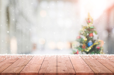Wood table top on blur with bokeh christmas tree background with snowfall - can be used for display or montage your products.