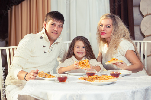 Family eating dinner at a dining table  Round table  pizza  orange  house made of wood