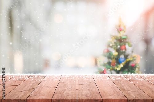 Wood table top on blur with bokeh christmas tree background with snowfall - can be used for display or montage your products.