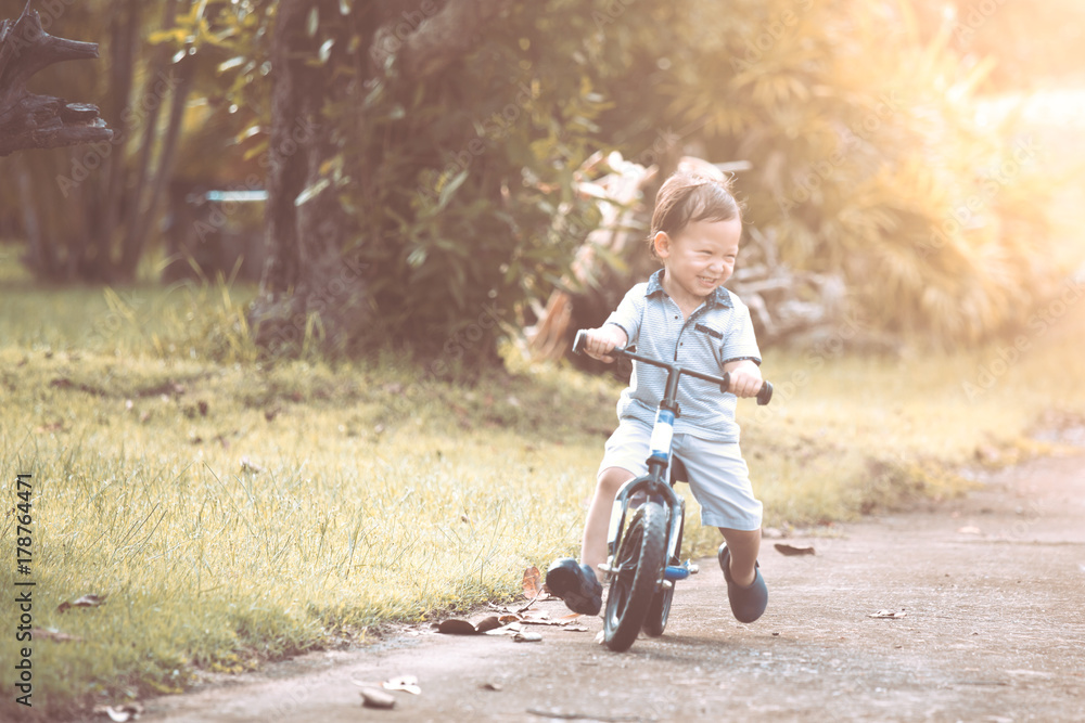 Cute asian little child boy having fun to ride his balance bike in the park in vintage color tone Cute asian little child boy having fun to ride his balance bike in the park in vintage color tone
