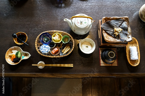Japanese ryokan breakfast appetizer dishes including  mentaiko, pickle, seaweed, bamboo shoot, hot plate, other side dishes,  green tea pot, cup and warm towel on wooden table