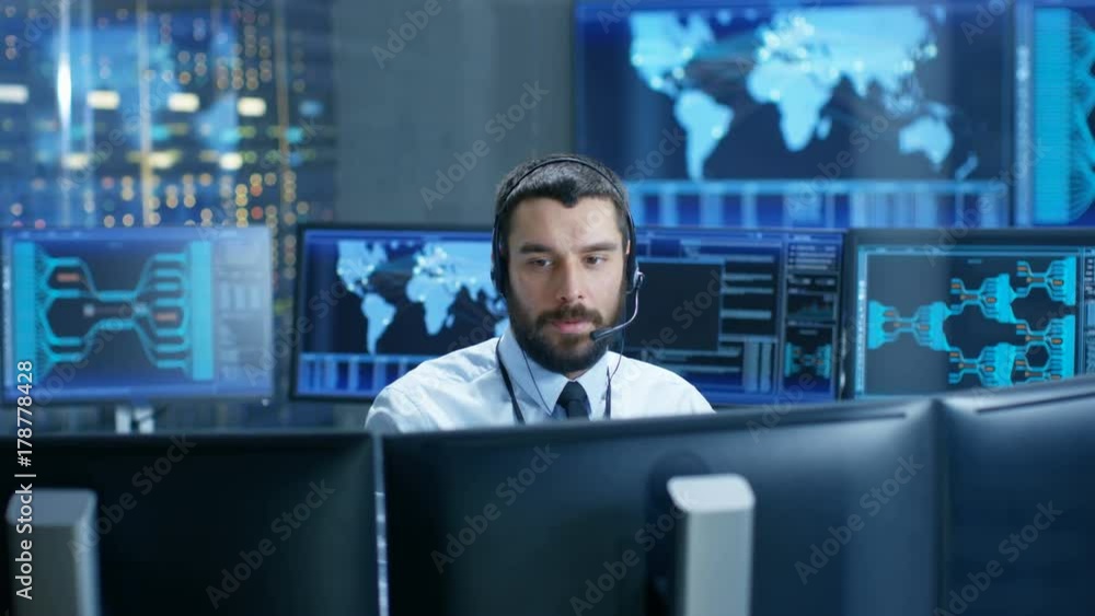 In the System Monitoring Room Dispatcher Speaks into Headset, Observers Proper Functioning of the Facility. He's Surrounded by Screen Showing Technical Data. In the System Monitoring Room Dispatcher Speaks into Headset, Observers Proper Functioning of the Facility. He's Surrounded by Screen Showing Technical Data.