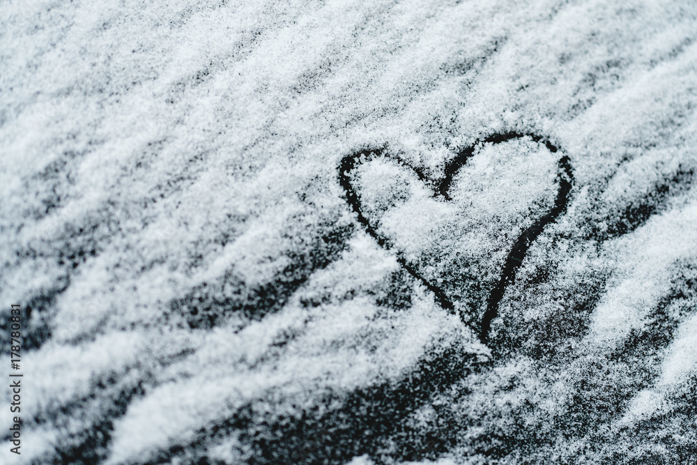 Heart symbol on a car windshield covered with fresh Christmas snow