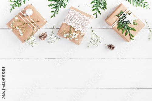 Christmas border. Christmas gifts, pine cones, gypsophila flowers, thuja branches on white wooden background. Flat lay, top view, copy space