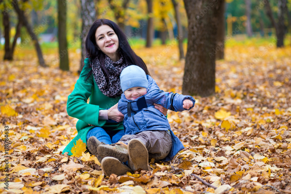 Mother with little son plays and smiles in park on background of colorful autumn fallen leaves Mother with little son plays and smiles in park on background of colorful autumn fallen leaves