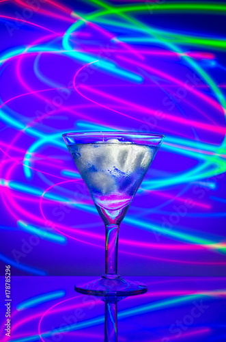 Glass with a cocktail with ice against a background of abstract illumination of colored neon