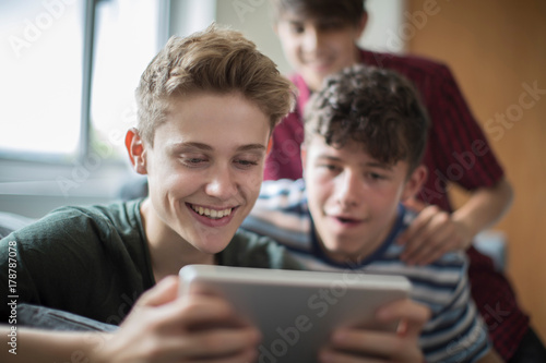 Three Teenage Boys Playing Game On Digital Tablet At Home