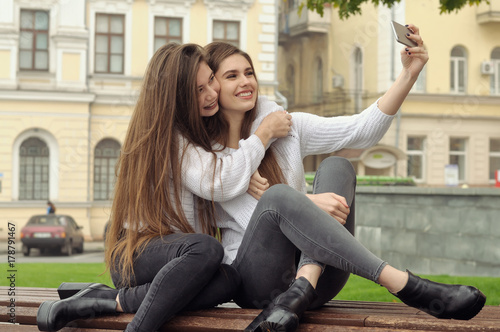 Two girlfriends hug and laugh as they make a selfie photo