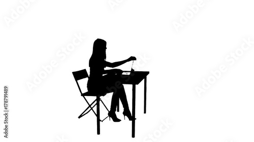 Woman sits down at the table and uses a laptop silhouette