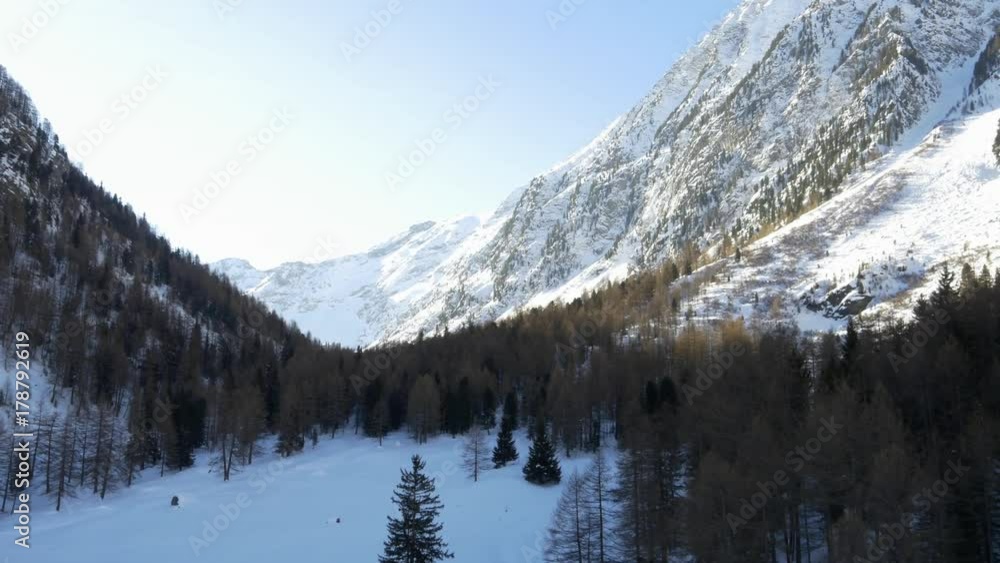 Winter aerial drone establisher over snowy forest woods valley under iced mountains.Snow in mountain nature outdoors.Forward flight. Travel exploring Alps. 4k top view video Winter aerial drone establisher over snowy forest woods valley under iced mountains.Snow in mountain nature outdoors.Forward flight. Travel exploring Alps. 4k top view video