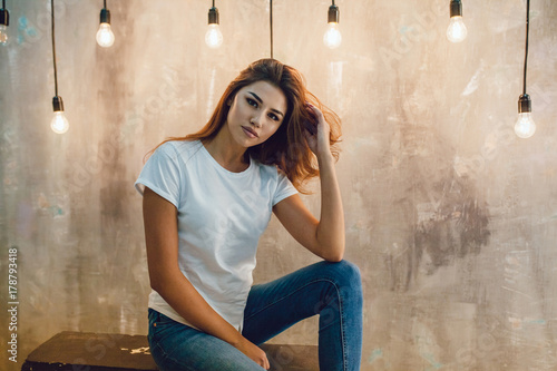 Sexy woman in a white T-shirt on a gray background with light bulbs. Mock-up. photo