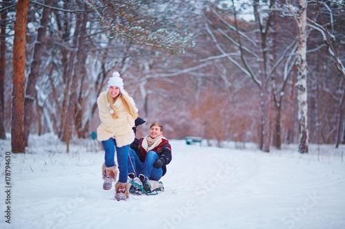 A happy couple is riding a sled in the snow in a park in the winter. St. Valentine's Day.