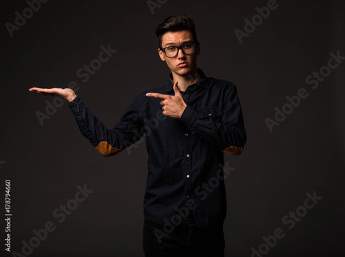 Young enigmatical man portrait of a confident businessman showing by hands on a black background. Ideal for banners, registration forms, presentation, landings, presenting concept.