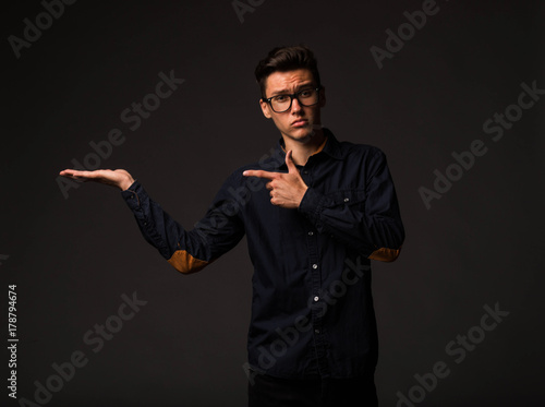 Young sexy man portrait of a confident businessman showing by hands on a black background. Ideal for banners, registration forms, presentation, landings, presenting concept.