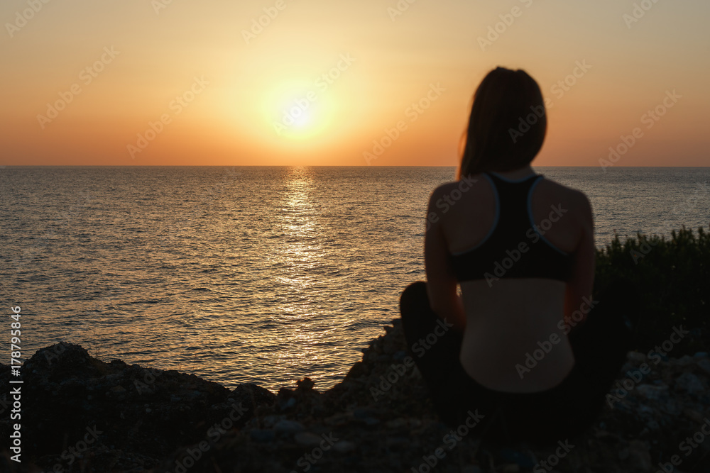 Sport girl meditating by the sea at sunset