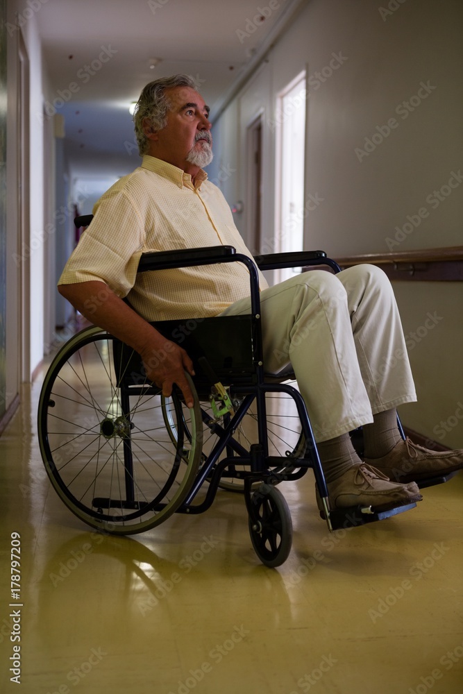 Thoughtful senior man sitting on wheelchair in corridor Thoughtful senior man sitting on wheelchair in corridor