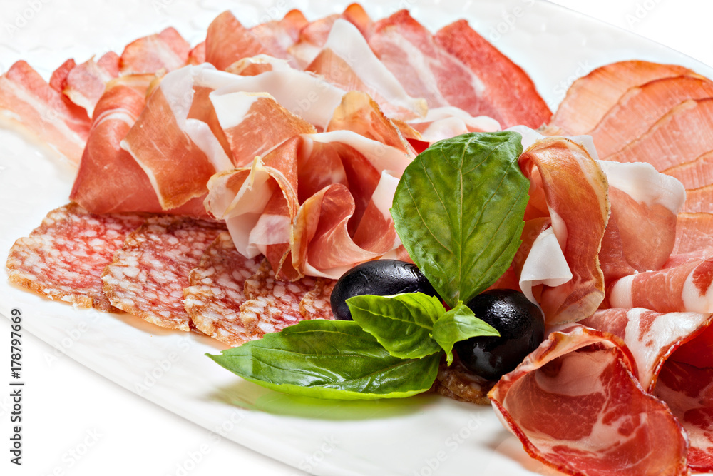 Sliced prosciutto, bacon, salami on a plate decorated leaf of basil and olive. Sliced prosciutto, bacon, salami on a plate decorated leaf of basil and olive.