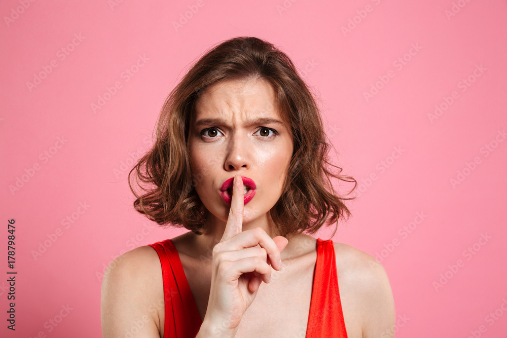 Close-up portrait of emotional pretty brunette woman showing silence gesture, looking at camera Close-up portrait of emotional pretty brunette woman showing silence gesture, looking at camera