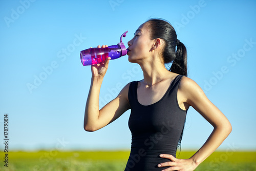 Asian sporty young woman drinking water outdoors