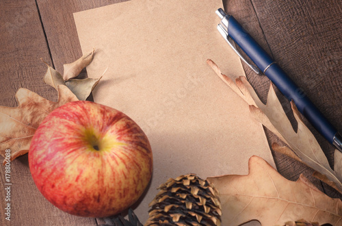 Frame of autumn leaves about page from notebook and pen with red apple