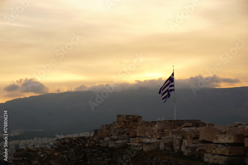 Obraz na płótnie Greek Flag over City with gorgeous Sunset Sky and clouds & mountains Background w salonie