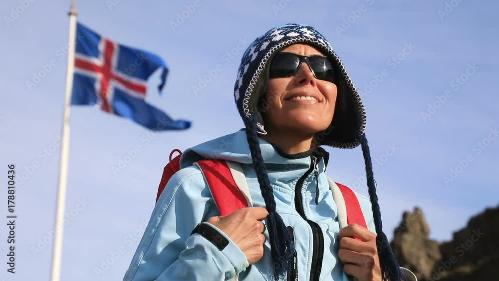 Portrait of travel woman with Iceland flag waving in wind against clear blue sky. Slow motion

