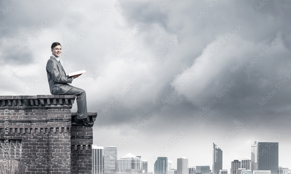 Man on roof edge reading book and cityscape at background Man on roof edge reading book and cityscape at background