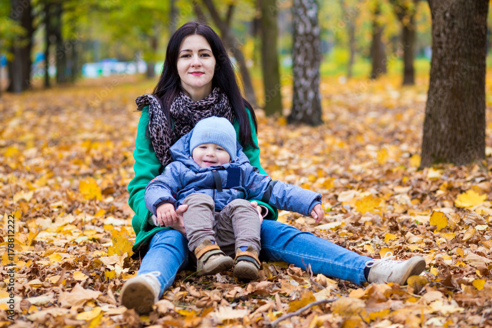 Mother with little son plays and smiles in park on background of colorful autumn fallen leaves Mother with little son plays and smiles in park on background of colorful autumn fallen leaves