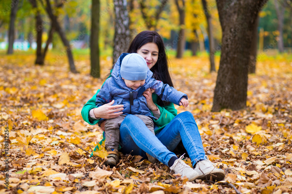 Mother with little son plays and smiles in park on background of colorful autumn fallen leaves