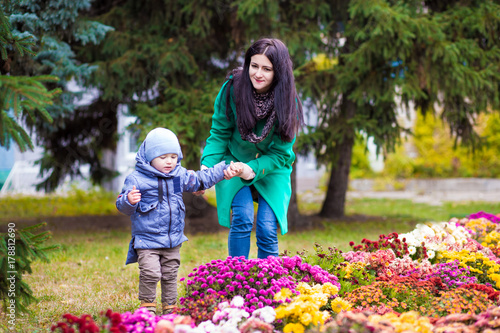 Mother with little son plays and smiles in park on background of colorful autumn fallen leaves