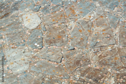 Background of an old fountain pond decorated with stones with coins thrown into water to make a wish come true, ripples and waves on water.