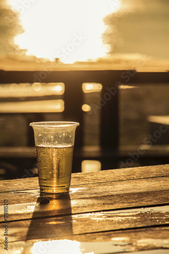 plastic glass which has beer inside on wooden table near beach