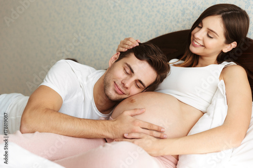 Smiling young pregnant wife lying in bed with her husband