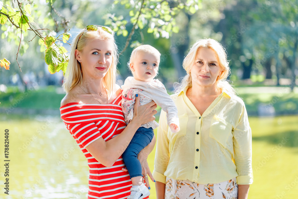 A happy family of three generations, mother, daughter, grandmother and little baby granddaughter, are standing together on the bridge of the river A happy family of three generations, mother, daughter, grandmother and little baby granddaughter, are standing together on the bridge of the river