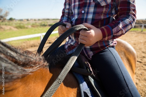 Mid section of girl riding a horse in the ranch
