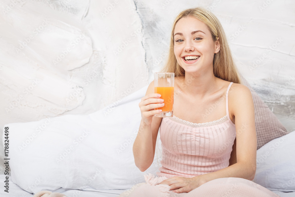 Cheerful woman drinking an orange juice sitting on her bed at home Cheerful woman drinking an orange juice sitting on her bed at home