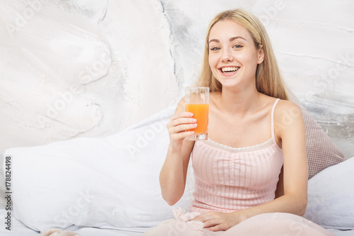 Cheerful woman drinking an orange juice sitting on her bed at home