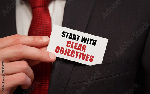 Businessman putting a card with text START WITH CLEAR OBJECTIVES in the pocket photo