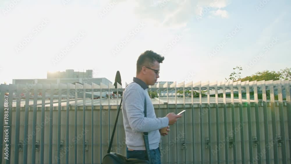 A young man walking and using a smartphone outside. Medium Dolly shot A young man walking and using a smartphone outside. Medium Dolly shot