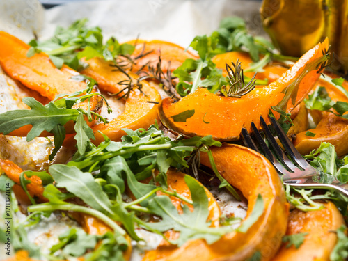 Baked pumpkin slices with arugula on baking tray. Fall food