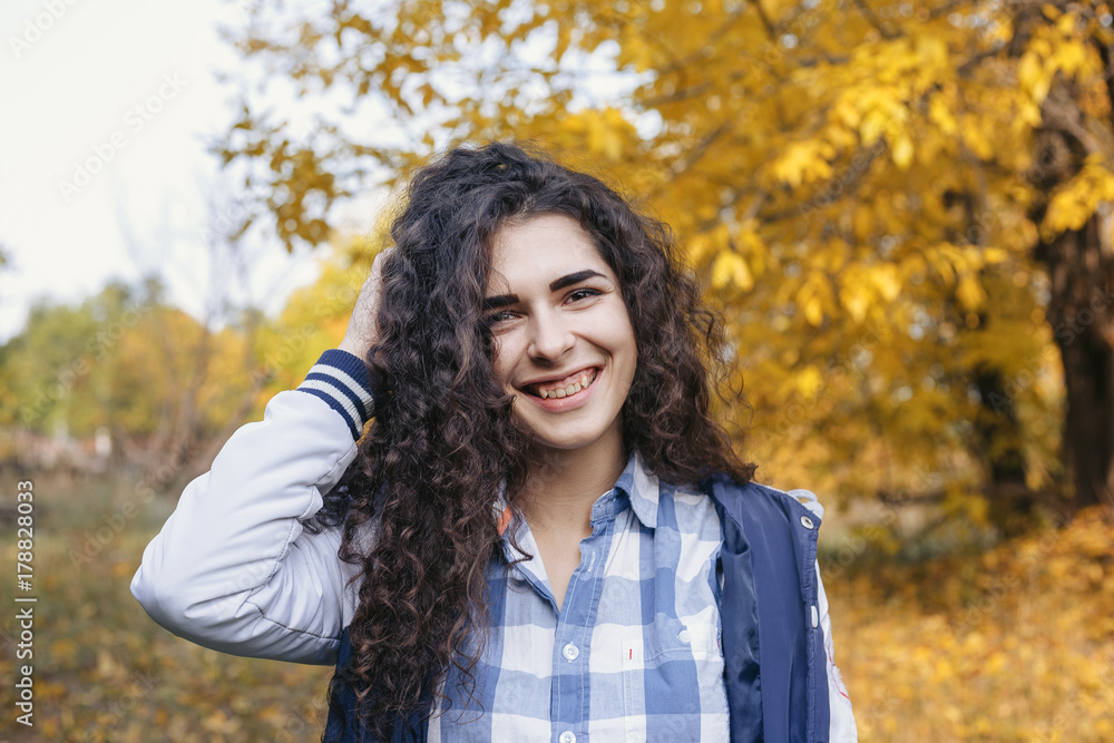 Pretty young woman with curly black hair and smiling face standing in autumn park and looking at camera. Pretty young woman with curly black hair and smiling face standing in autumn park and looking at camera.