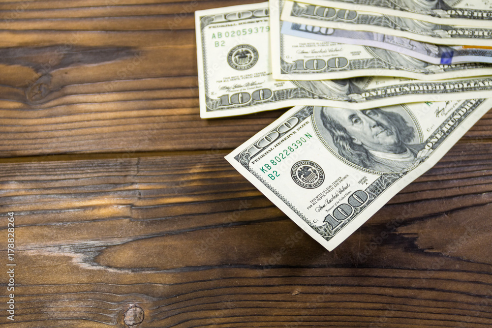 One hundred dollars bills on wooden desk One hundred dollars bills on wooden desk