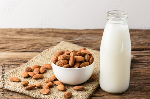 Peeled almonds with bowl and Bottle of almond milk on rustic wooden