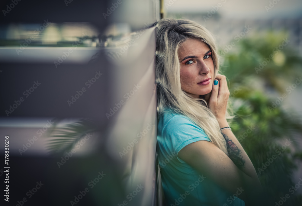 Fototapeta premium Portrait of a beautiful blonde closeup. Wearing a turquoise t-shirt. Arms tattooed. The concept of modern fashion.