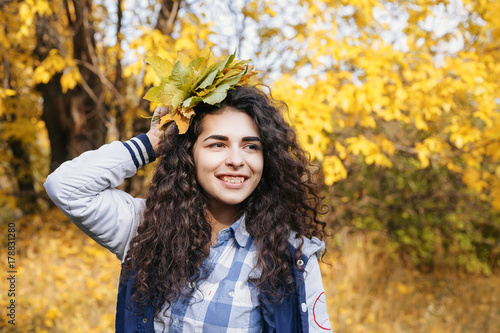 Happy curly woman holding bouquet of autumn leaves in hand and posing in autumn park.