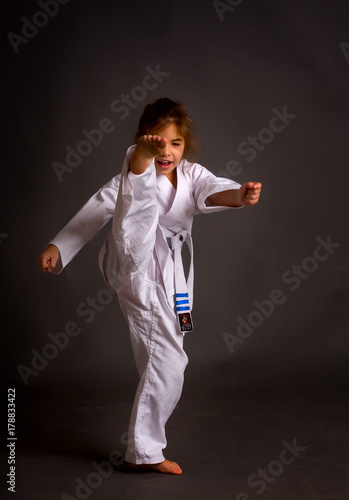 A little girl karate in a white belt, but already received three patches performs kata